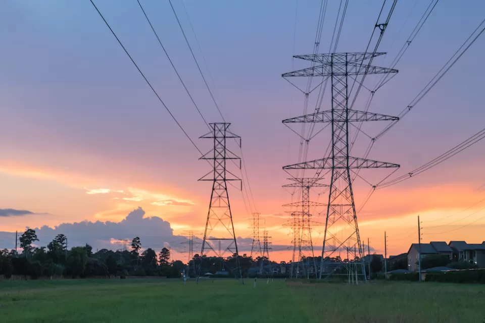 Electricity towers against sunset sky with green trees in background.